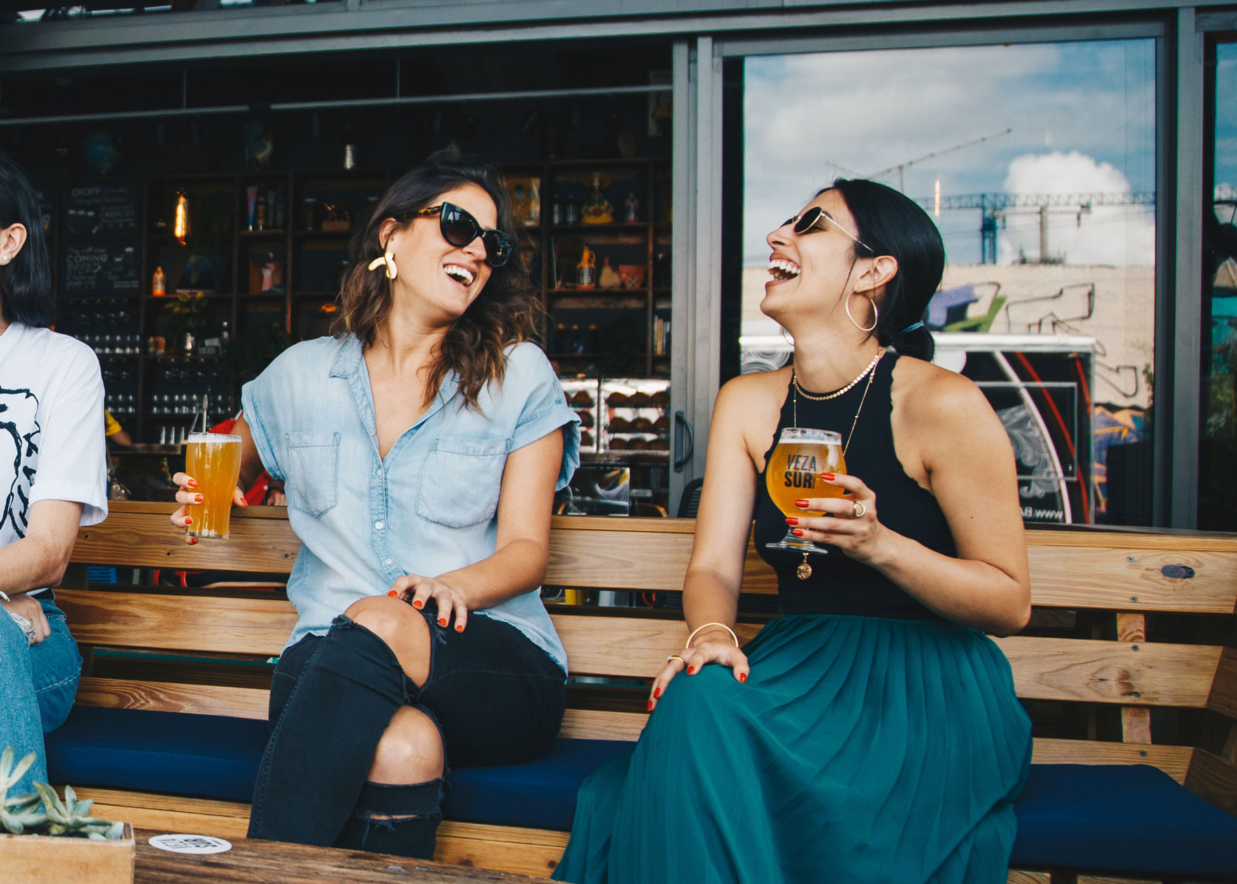 Women friends laughing, drinking craft beer and relaxing at outdoor pub